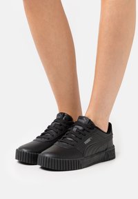 Musta nahkakengät kumipohjalla, tekstuuriset yksityiskohdat, nauhakiinnitys ja Puma-logo kielellä ja sivussa.