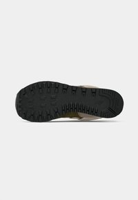 Semelle d'une chaussure beige et vert olive montrant une bande de roulement en caoutchouc noir texturé conçue pour l'adhérence et la durabilité.