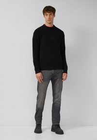 Czarny sweter dzianinowy z okrągłym dekoltem, w zestawieniu z ciemnoszarymi dżinsami i czarnymi sznurowanymi butami. Minimalistyczny design, gładka tekstura.