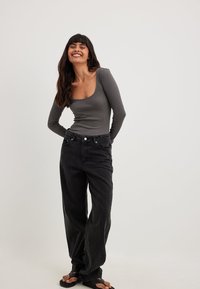 Grå ribbad långärmad topp med rundad halsringning, tillsammans med stora svarta denimjeans och svarta flip-flops. Enkelt och avslappnat outfit.