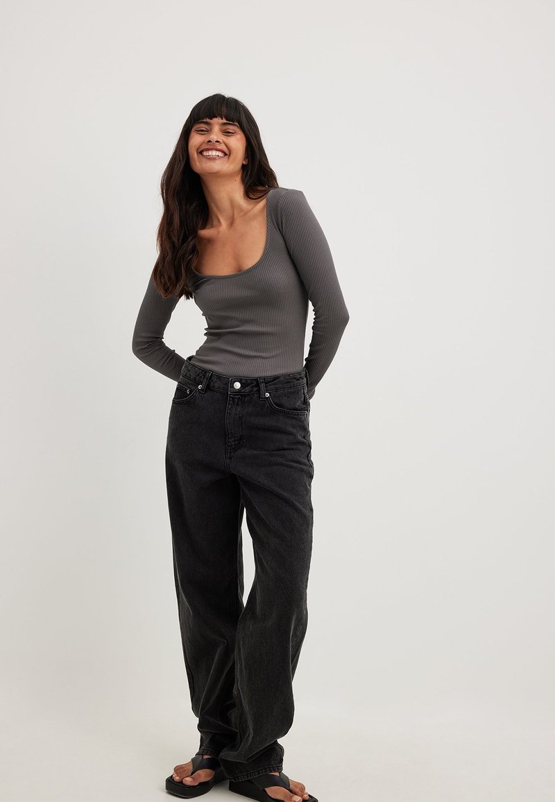 Grå ribbad långärmad topp med rundad halsringning, tillsammans med stora svarta denimjeans och svarta flip-flops. Enkelt och avslappnat outfit.