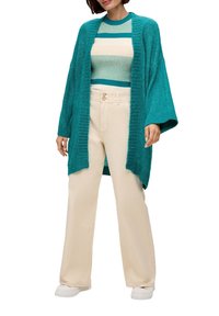 Türkisfarbener, gestrickter langer Cardigan mit offenem Front, kombiniert mit einem gestreiften Pullover in Türkis und Beige, dazu beigefarbene weite Hose und weiße Sneaker.