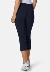 Marineblaues Cropped-Hose mit glatter Textur, tailliertem Schnitt und mittlerem Bund, kombiniert mit weißen Schuhen mit silbernen Akzenten.