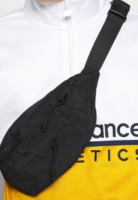 Czarna nylonowa torebka crossbody o zaokrąglonym kształcie i regulowanym pasku, z zapięciem na sznurek i teksturowanym materiałem.