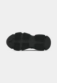 Semelle de chaussure de sport noire avec des motifs de traction en caoutchouc texturé et des rainures multidirectionnelles pour une meilleure adhérence. Bout arrondi et conception supportive.