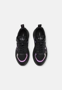 Scarpe da ginnastica nere con pannelli in rete, dettagli viola e suole testurizzate. Presentano un design con lacci e un logo prominente sul lato.