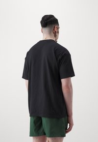 Svart bomullströja med avslappnad passform, korta ärmar och rundad nacke, tillsammans med gröna shorts. Enkel, lätt design.