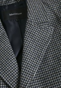 Grau und marineblaues Hahnentrittmuster-Blazer mit Reverskragen, klaren Linien und einem glatten Innenfutter. Logostickerei innen am Kragen sichtbar.