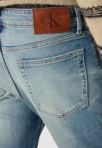 Svijetloplave traperice s kožnom oznakom Calvin Klein, vidljivim šavovima i dva stražnja džepa s izblijedjelom teksturom.