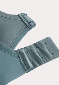 Brahm i mjukt blått tyg med slät textur. Funktioner justerbara axelremmar och hake-och-öga stängning med fyra öglor för passformjustering.