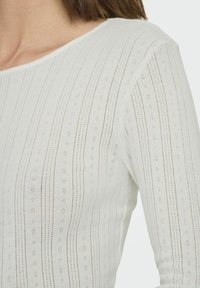 White knitted top featuring vertical stripes with small holes. Smooth texture, wide neckline, and fitted design. Light and breathable fabric.