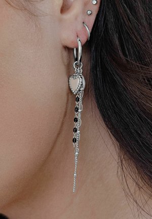 Silberne Creolen mit einem Herzanhänger und herabhängenden Ketten mit schwarzen Perlen. Glatte Textur und glänzendes Finish.