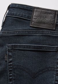 Mörka denimjeans med en svart läderpatch i ryggen med präglad logotyp. Inkluderar detaljer i bakfickans söm och sidetikett.