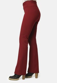 Mujer con pantalones de campana de cintura alta en un rojo oscuro con detalles de botones, combinados con botines negros de tacón.