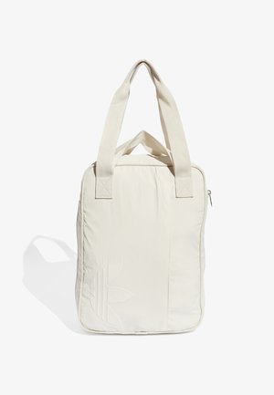 Sac fourre-tout rectangulaire beige avec deux larges anses, logo subtil embossé à l'avant et fermeture éclair en haut, projetant une ombre douce sur fond blanc.