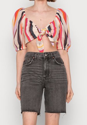 Gekürztes, mehrfarbig gestreiftes Oberteil mit puffigen Ärmeln und einem Knoten-Detail vorne, kombiniert mit hochgeschnittenen, ausgefransten schwarzen Jeansshorts.