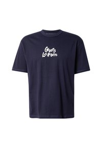 Camiseta de algodón azul marino con cuello redondo y mangas cortas. Presenta un texto gráfico blanco "Guess Los Angeles" en la parte delantera.