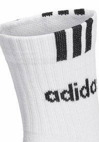 Calcetín deportivo blanco con el logo negro de Adidas y tres rayas negras cerca del borde superior, con textura acanalada visible.