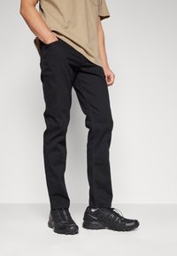 Svarta byxor och svarta sportskor. Byxorna är slim-fit med en slät yta; skorna har en strukturerad ovandel och en hållbar sula.