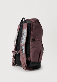 Σακίδιο πλάτης μαρονού χρώματος με μαύρες λεπτομέρειες, επενδεδυμένους ιμάντες ώμου, αντανακλαστικές λεπτομέρειες, πλαϊνή τσέπη και χειρολαβή στην κορυφή για εύκολη μεταφορά.