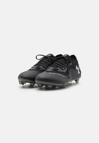 Scarpe da football nere con superficie texturizzata, design con lacci e un prominente logo Under Armour. Suola in gomma nera con tacchetti per migliorare la trazione.