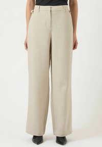Béžové široké kalhoty s texturovanou látkou, vysokým pasem, bočními kapsami a kovovými doplňky v pase. Kombinovány s černými podpatky.