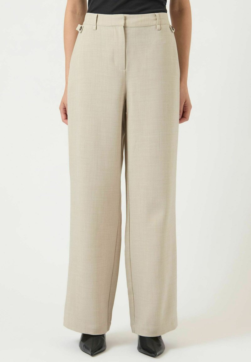 Béžové široké kalhoty s texturovanou látkou, vysokým pasem, bočními kapsami a kovovými doplňky v pase. Kombinovány s černými podpatky.