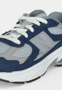 Γκρι και ναυτικό μπλε αθλητικό παπούτσι New Balance με λευκά κορδόνια, πλέγματα και μαξιλαρωτή λευκή σόλα σε ανοιχτό φόντο.