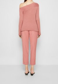 Un pull rose dénudé sur les épaules avec des manches longues, associé à un pantalon tapered rose clair et des sandales noires à enfiler, présenté de dos.