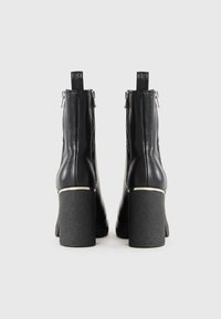 Bottes noires en cuir au niveau de la cheville avec un talon épais et texturé, des fermetures éclair sur les côtés et des languettes pour un enfilage facile. Fini lisse et poli.
