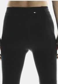 Leggings de sport noirs avec une texture lisse et extensible, dotés d'une poche zippée à l'arrière et de coutures plates pour plus de confort.
