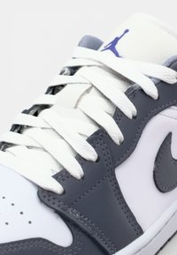 Baskets blanches et grises avec une tige en cuir lisse, des lacets blancs plats et un logo Nike gris. Dotées d'une languette rembourrée et d'un bout perforé.