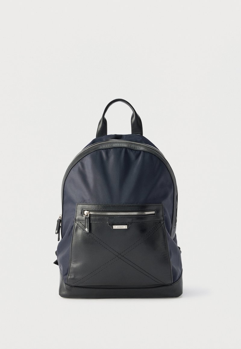 Σχολική τσάντα σε ναυτικό μπλε και μαύρο χρώμα με εμπρόσθια τσέπη με φερμουάρ, χερούλι στην κορυφή και ασημένιες λεπτομέρειες φερμουάρ, σε λευκό φόντο.