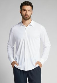 Witte langemouwen overhemd met knopen en een standaardkraag, gladde textuur en rechte snit. Gekozen over donkere broek.