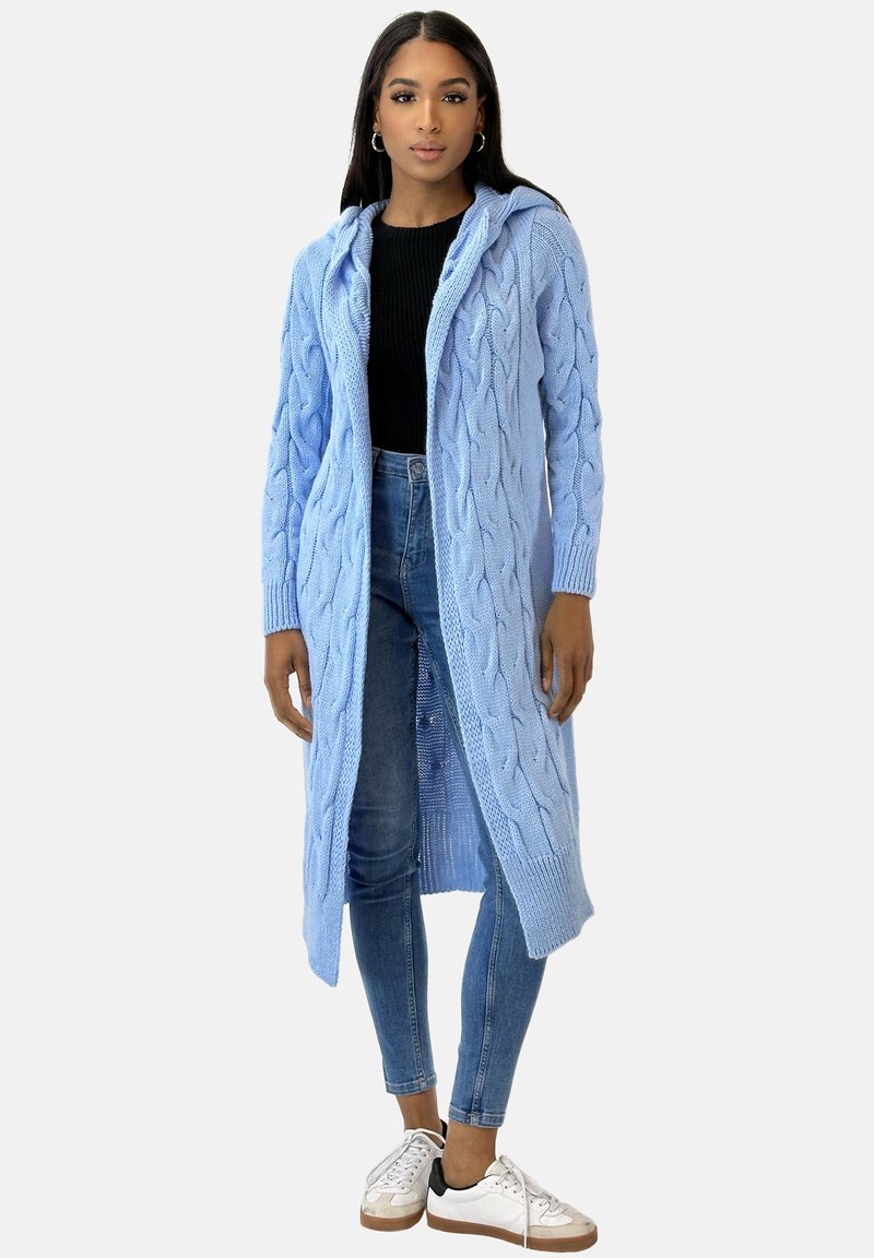 Ljusblå stickad cardigan med huva, med kabelmönster och långa ärmar, bärs över en svart topp och blå jeans, ihop med sneakers.