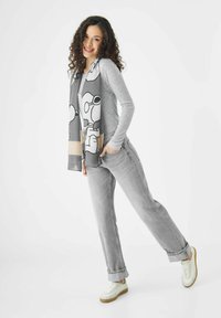 Grijze longsleeve shirt gecombineerd met lichtgrijze jeans en witte sneakers. Een gemusterde grijze sjaal toont cartoonfiguren in zwarte omtrekken.