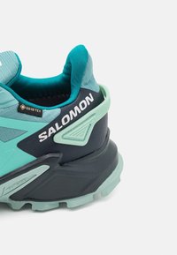 Talons de chaussure de randonnée Salomon bleu sarcelle et noir avec étiquette GORE-TEX, soutien renforcé de la cheville et semelle extérieure robuste pour une utilisation en extérieur.