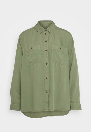 Light green button-up shirt made of soft fabric, featuring two chest pockets and brown buttons. The design has a relaxed fit and curved hem.