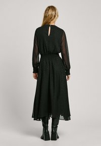 Mustat maxi-mekko, jossa on pitkät läpinäkyvät hihat, smokkatussa vyötärössä on avainaukko takana sekä huomaamaton pilkkuja koko sivussa.