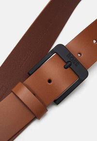 Brauner Leder Gürtel mit glatter Textur, ausgestattet mit einer rechteckigen schwarzen Metall-Schnalle, die mit "BOSS" graviert ist, sowie mehreren Einstelllöchern.