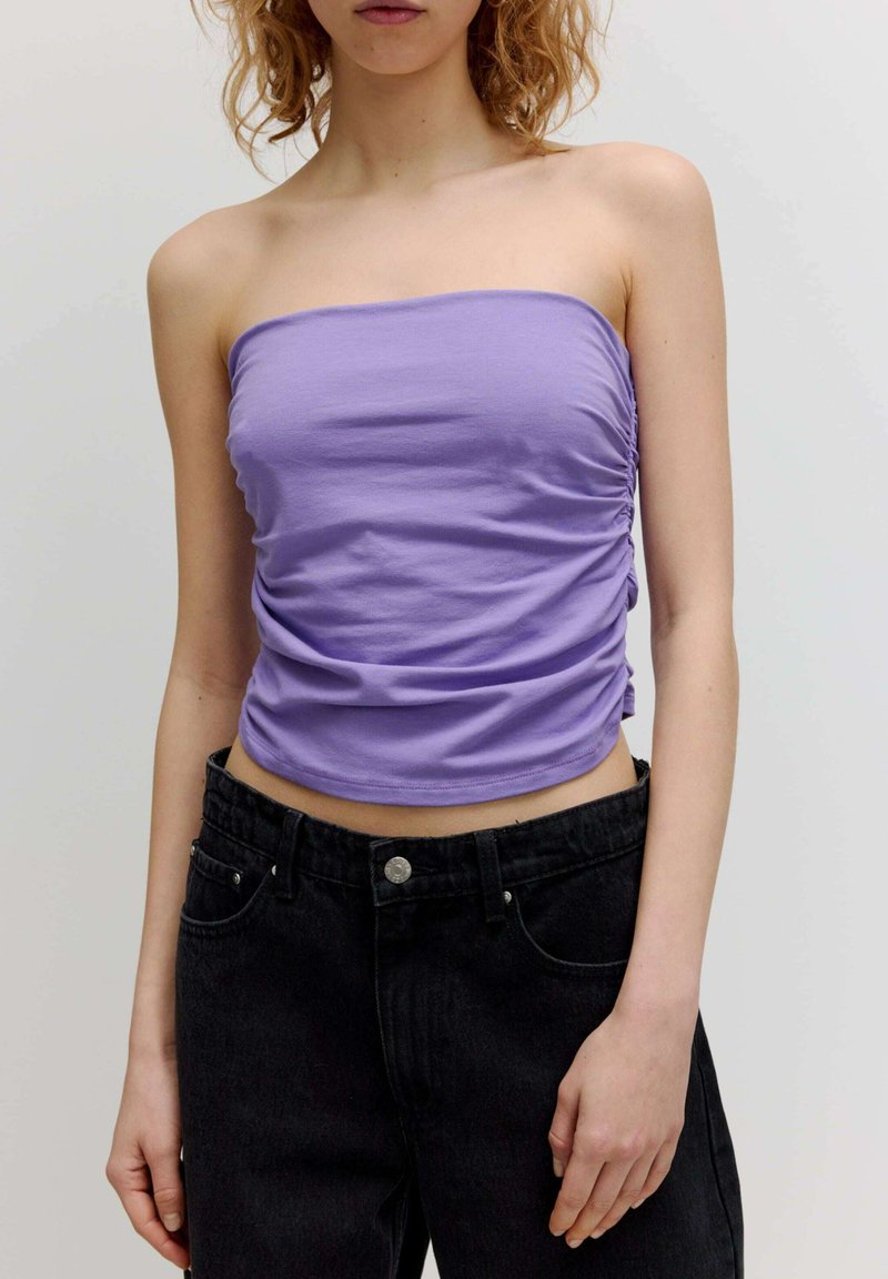 Blausfarbener trägerloser Top aus glattem Stoff mit gerafften Seitendetails, kombiniert mit hochtaillierten schwarzen Jeans. Fokus auf Textur und Farbe.