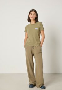 Olivovo zelené, štruktúrované tričko s krátkym rukávom a modrým logom. Kombinované s voľne strihanými olivovými nohavicami a modrou obuvou. Jednoduchý dizajn.