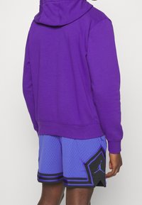 Sweat à capuche violet avec poche kangourou, associé à un short en mesh bleu clair avec un accent noir et un détail logo.