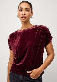 Bordeaux velour t-shirt med løs pasform, opkrøllede korte ærmer og rund hals. Glat tekstur med en subtil glans.