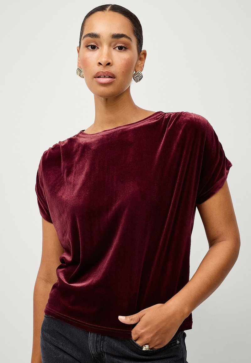 Bordeaux velour t-shirt med løs pasform, opkrøllede korte ærmer og rund hals. Glat tekstur med en subtil glans.