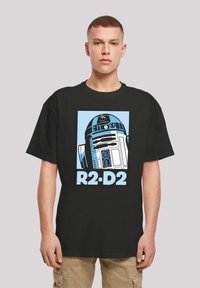 Svart bomull T-skjorte med et grafisk motiv av R2-D2 i blått og hvitt, med teksten "R2-D2" under designet. Korte ermer og løs passform.