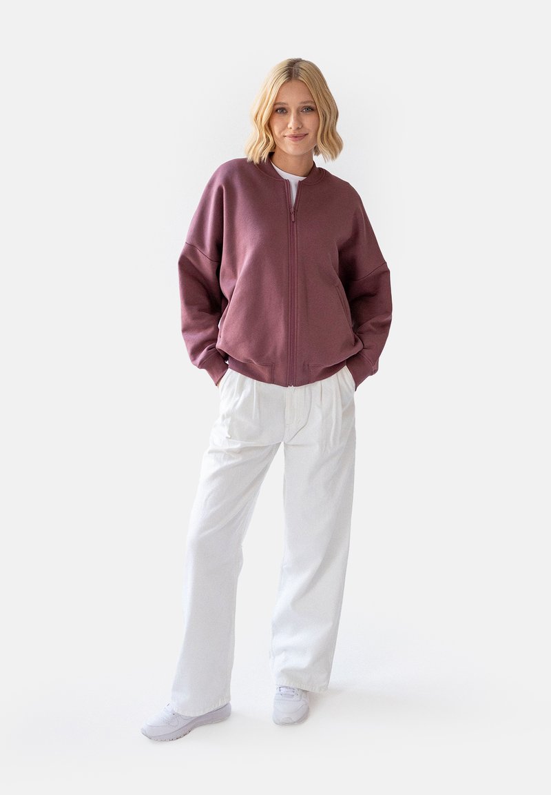 Bordowy sweatshirt na zamek błyskawiczny z opadającymi ramionami, w połączeniu z luźnymi białymi spodniami i białymi sneakersami. Miękka tkanina i swobodny krój.