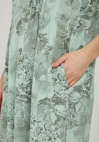 Vaaleansininen mekko, jossa on harmaa kukkakuosi, rento leikkaus, sivutaskut ja pehmeä, teksturoitu kangas.