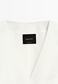 Witte linnen blouse met een V-hals en korte mouwen, voorzien van een zwart label met "Massimo Dutti" en verzorgingsinstructies.