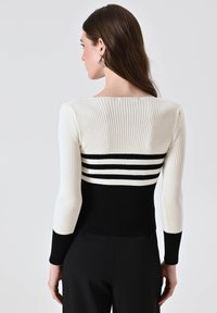 Maglione a righe in bianco e nero con un design aderente, maniche lunghe e dettagli a strisce orizzontali attorno alla vita. Tessuto liscio.